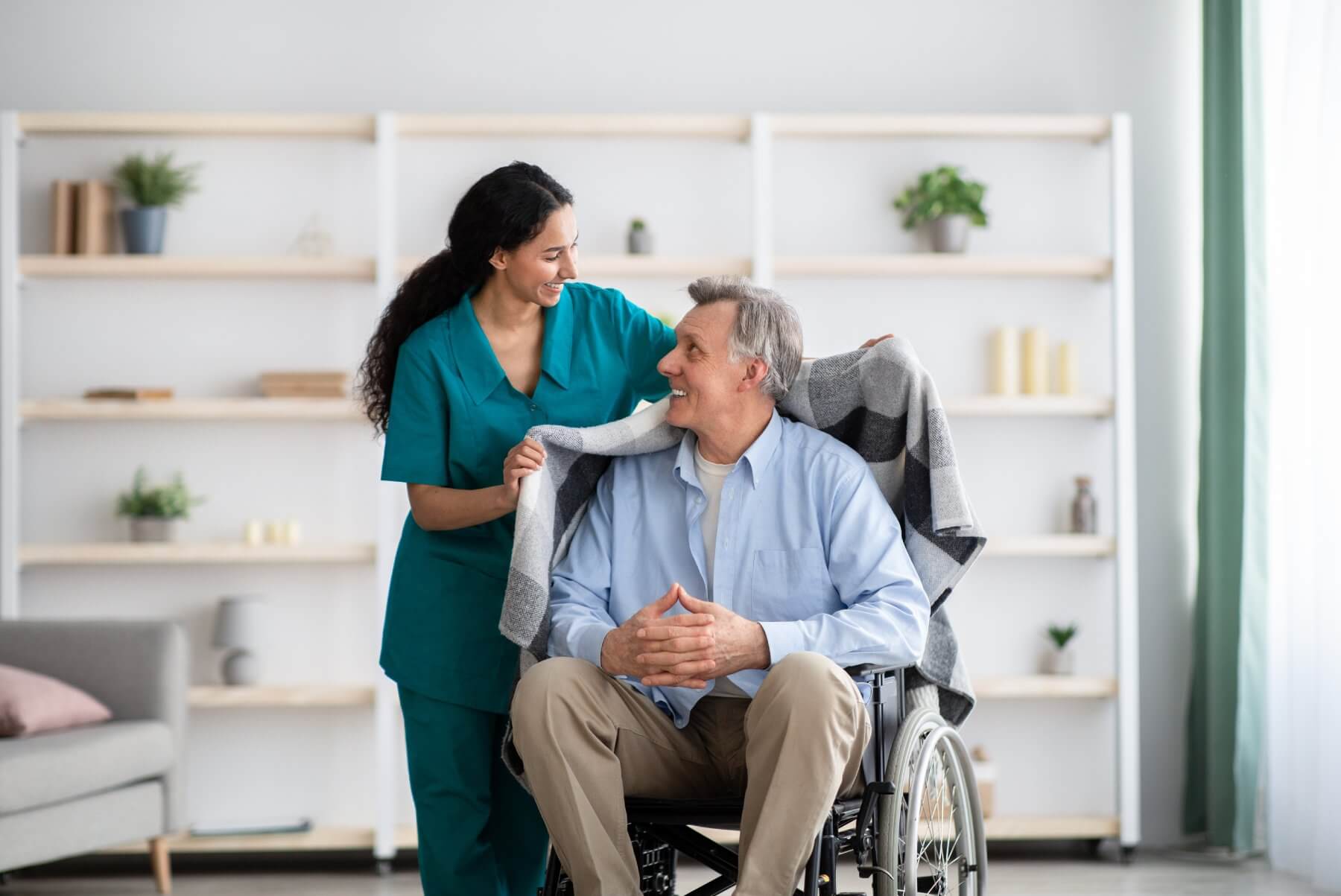 Nurse covering elderly man in wheelchair with a warm blanket
